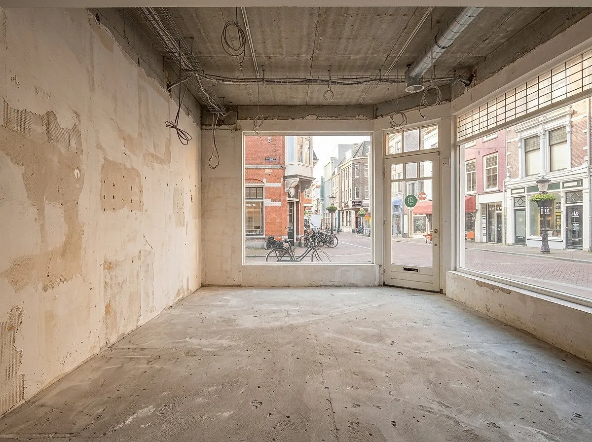 Dezelfde winkelruimte in casco: leeg, deur en pui rechts, wachtend op de renovatie.